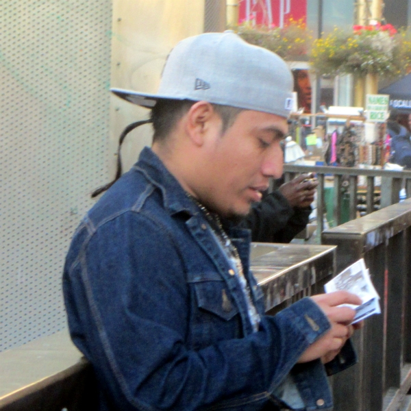 YOUNG MAN READS SPANISH TRACT AT 5TH ST AND MARKET.
