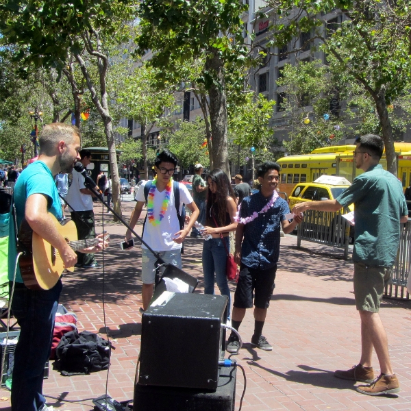 CAL SINGS AND JACOB PASSES OUT TRACTS AT 5TH AND MARKET. THE RAINBOW NECKLACES ARE FOR GAY PARADE.